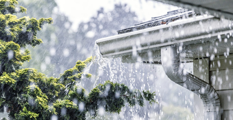 Gouttière qui déborde sous une pluie battante, descente d’eau pluviale au premier plan