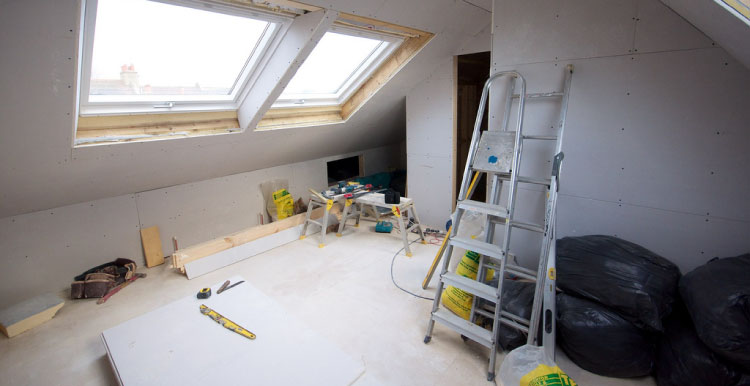 Combles en cours d’aménagement : plaques de plâtre, deux fenêtres de toit et escabeau