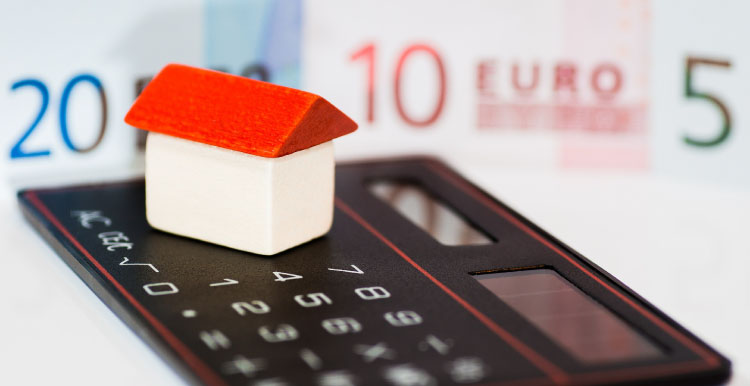 Maison miniature posée sur une calculatrice devant des billets en euros