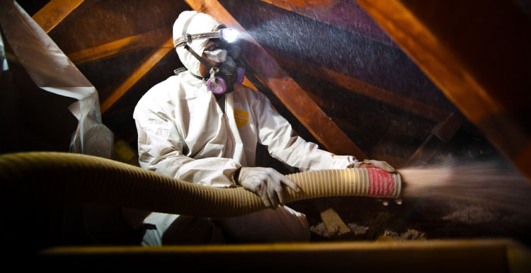 Opérateur en combinaison, masque et lampe frontale, projetant de la ouate de cellulose