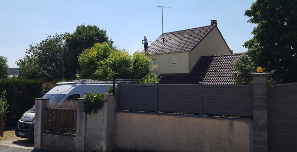 Technicien démoussant la toiture d’une maison, utilitaire garé devant le portail