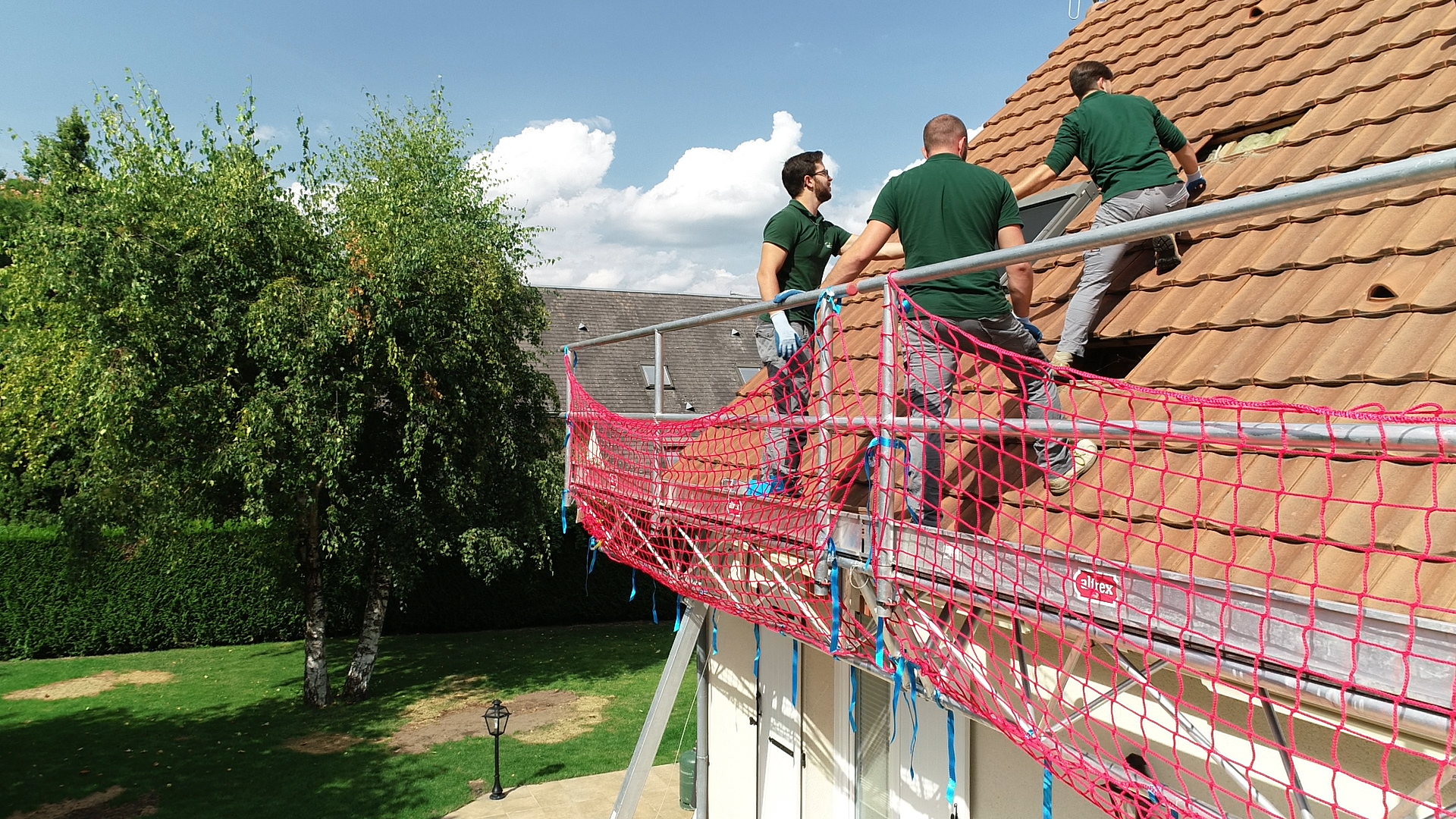 Trois compagnons Isol’Centre sur le garde-corps d’un chantier de toiture, filet de sécurité tendu